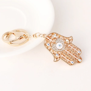 Porte-clés Main de Fatma doré avec œil de cristal et motif cœur sur plateau blanc