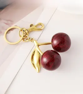 Detailed view of dark red glitter cherry keychain with golden leaf and metal ring hook