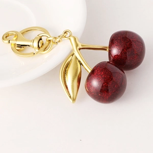 Sparkling dark red cherry fruit keychain with gold hardware on minimalist white background