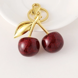 Glittery dark red cherry fruit keychain with golden leaves on a white ceramic plate