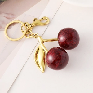 Sparkling dark red cherry keychain with golden leaves and lobster clasp on white background