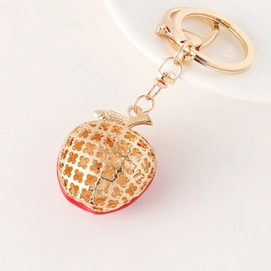 Porte-clés pomme dorée avec fond en émail rouge et motif floral ajouré sur fond blanc