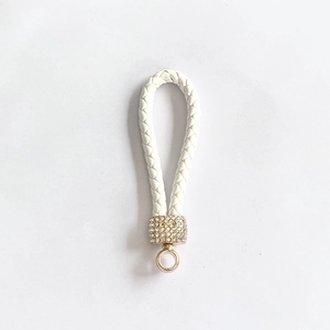Detail of white woven leather keychain with gold cylindrical rhinestone encrusted accents