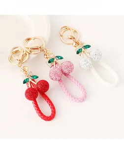 Détail de porte-clés cerises en cristal 3D avec lanières en cuir tressé rouge rose et blanc