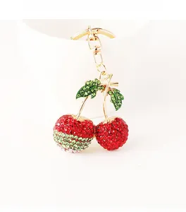 Detail of red and green rhinestone cherry keychain with gold metal clasp on white bowl