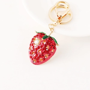 Sparkling strawberry keychain with red crystals and gold metal clasp on a white plate