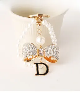 Detail of a pearl bow keychain with a golden letter D hanging on a white ceramic mug