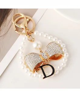 Macro detail of pearl keychain featuring sparkling crystal bow and black D pendant charm
