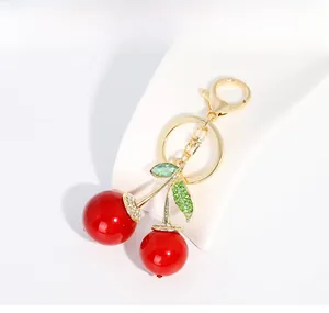 Gros plan d'un porte-clés cerise avec perles rouges, strass verts et métal doré brillant