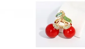 Détail d'un pendentif cerise avec fruits rouges, tige dorée et cristaux verts brillants
