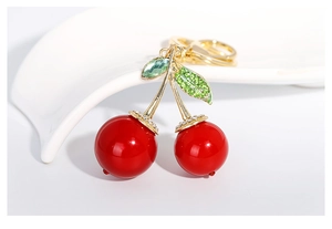Vue macro du porte-clés cerise avec feuilles dorées et strass verts sur plateau blanc