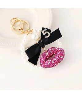 Detail of luxury keychain with rhinestone lips, ribbon bow, and pearl ring on white tray