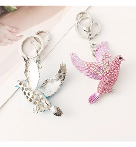 Close-up of sparkling bird keychains in silver and pink with rhinestones and metal rings