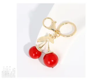 Détails d'un porte-clés cerise rouge avec feuilles dorées et strass blancs brillants