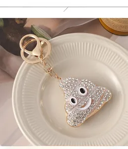 Porte-clés émoji crotte doré avec strass blancs brillants exposé sur un plateau céramique