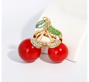 Détail du pendentif cerise rouge avec feuilles en strass verts et cadre doré