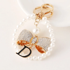 Elegant pearl keychain with rhinestone bow and black letter D pendant on white background