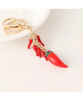 Detail of red chili keychain with gold hardware on a white ceramic plate background