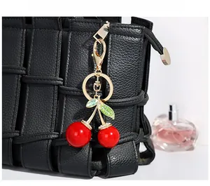 Détail d'un porte-clés cerise rouge avec feuilles en cristal sur un sac en cuir tressé