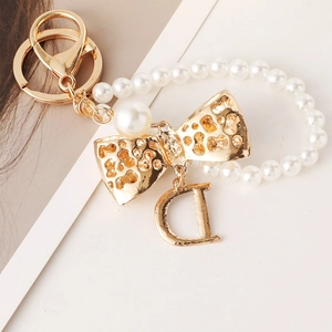 Elegant gold bow keychain with white pearls and a large letter D charm pendant