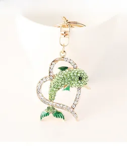 Detail of dolphin heart keychain with green rhinestones and gold plating on white cup