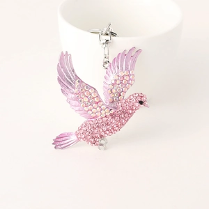 Exquisite rhinestone bird keychain with pink and purple crystals on a ceramic cup