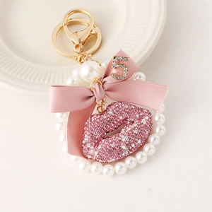 Pink bow keychain with pearl ring and sparkling lip pendant on a white ceramic plate
