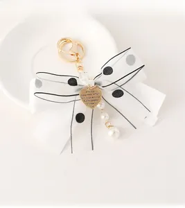 Detailed close-up of a chiffon bow keychain with pearls and heart charm on a porcelain plate