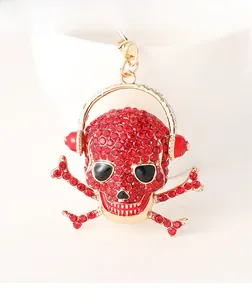 Close-up of gold skull keychain with red rhinestones and headphones on white background