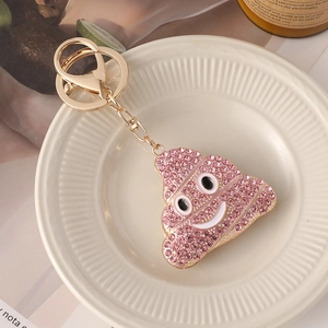 Porte-clés émoji crotte en strass rose avec anneau en métal doré posé sur un plateau en céramique