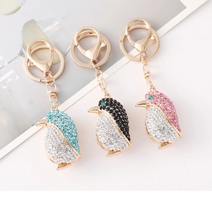 Detalle de tres llaveros de pingüino con diamantes de imitación brillantes en azul y rosa