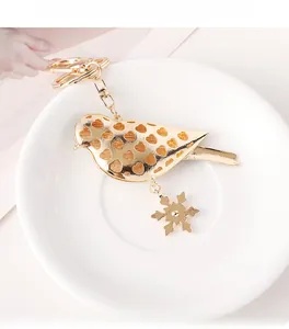 Nahaufnahme von goldenem Vogel-Schlüsselanhänger mit Herzdekor und Schneeflocken-Anhänger