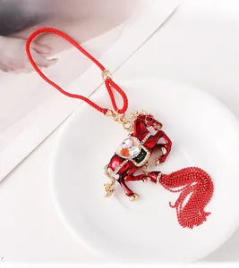 Detail of red enamel horse pendant with golden edges, colorful rhinestones and beaded tassels