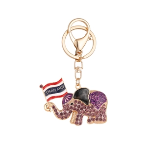 Golden elephant keychain with purple rhinestones holding a Thailand flag on white background
