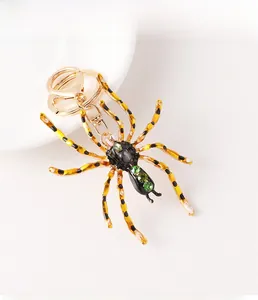 Détail d'un porte-clés araignée dorée avec strass verts et pattes tachées de jaune