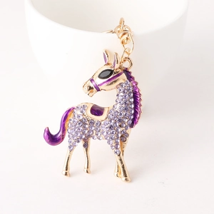Golden horse keychain with purple rhinestones and enamel hanging on a white ceramic cup
