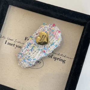 Détail d'une pince à cheveux en tweed multicolore avec plaque métallique cœur gravée