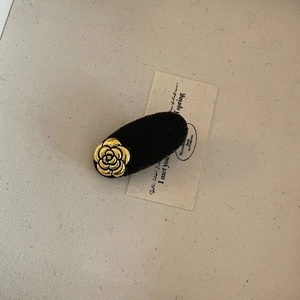 Detail of a brown velvet hair clip with a golden metallic camellia flower on linen