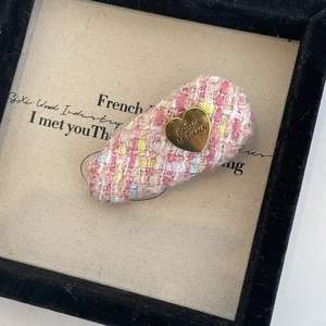 Détail d'une barrette en tweed rose avec un pendentif en cœur doré et une gravure