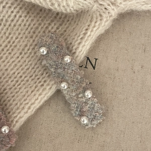 Close-up of pink tweed hair clip with white faux pearls on soft knitted background