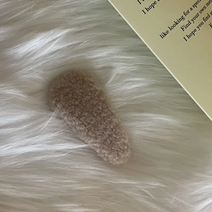 Close-up of a brown plush cream puff hair clip on a soft white faux fur background