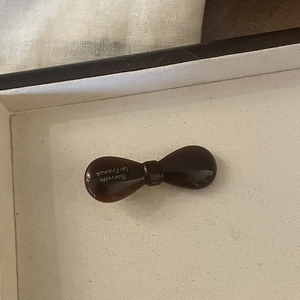 Dark brown acetate bow hair clip with gold logo lettering on a cream jewelry box