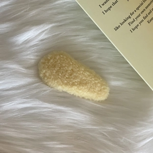 Detailed close-up of warm beige plush hair clip with soft lamb wool texture on fuzzy background