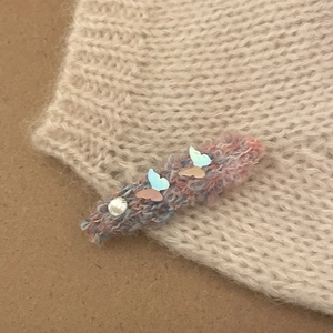 Macro view of a knitted hair clip featuring iridescent butterflies and a crystal rhinestone