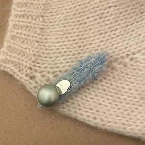 Detail of blue knitted hair clip with green pearl bead and Princess engraved metal tag