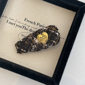 Détail d'une barrette en tricot français avec un charm coeur doré sur fond beige