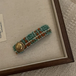 Détail de la pince à cheveux en tweed menthe et orange avec un bouton doré vintage