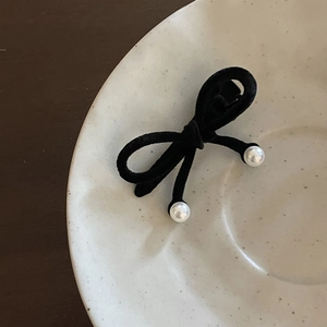 Black velvet bow hair clip with faux pearl pendants on a ceramic plate background