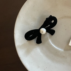 Detailed macro view of black velvet bow hair clip featuring a centered white pearl