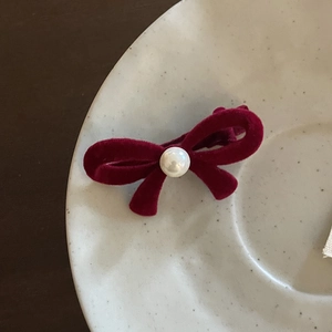 Detail of red velvet bow hair clip with center pearl on a ceramic tray macro view
